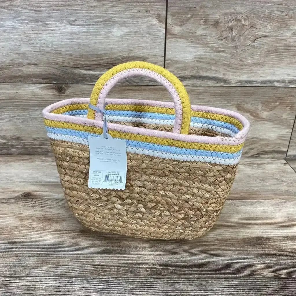 Front view of seagrass woven basket with pastel pink, yellow, and blue striped rim and coiled rope handles on wood background