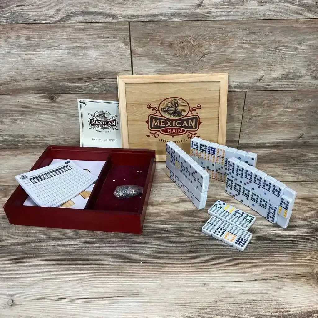 Top-down view of Deluxe Wooden Mexican Train Dominoes showcasing wooden box dominoes scorepad train marker and instructions on wood plank floor