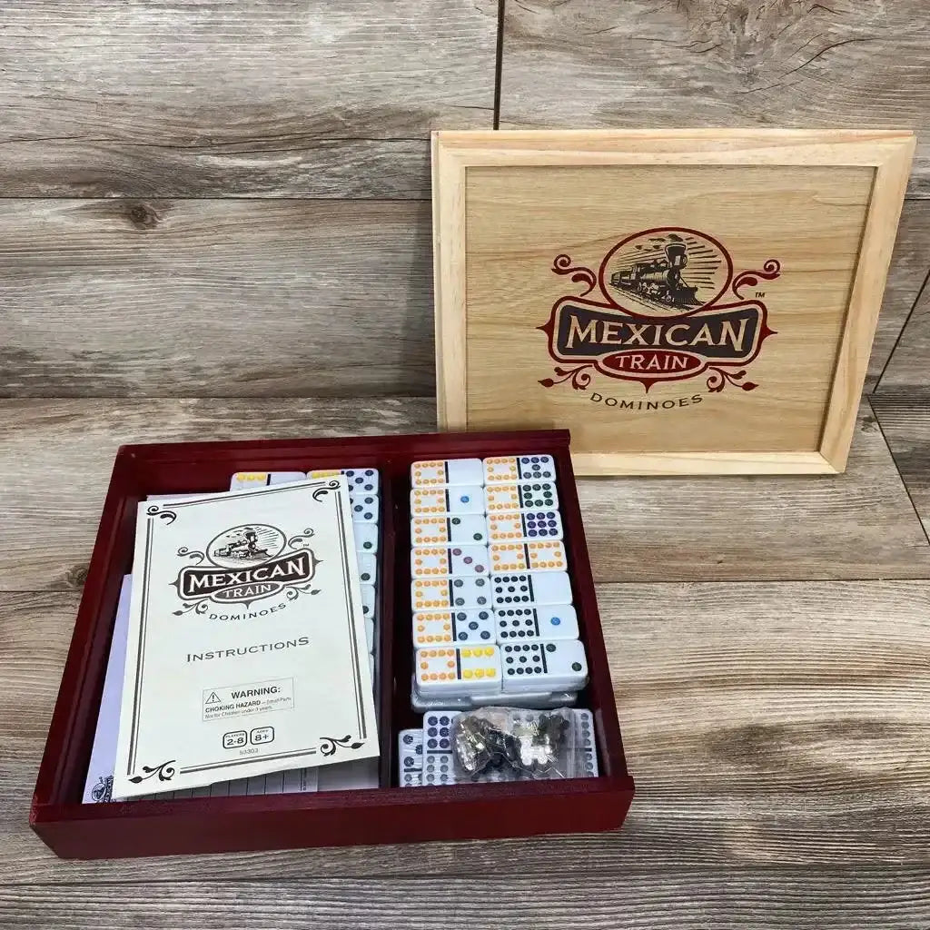 Top view of Deluxe Wooden Mexican Train Dominoes set showcasing wooden box with engraved lid instructions booklet and colorful domino tiles on wood plank background