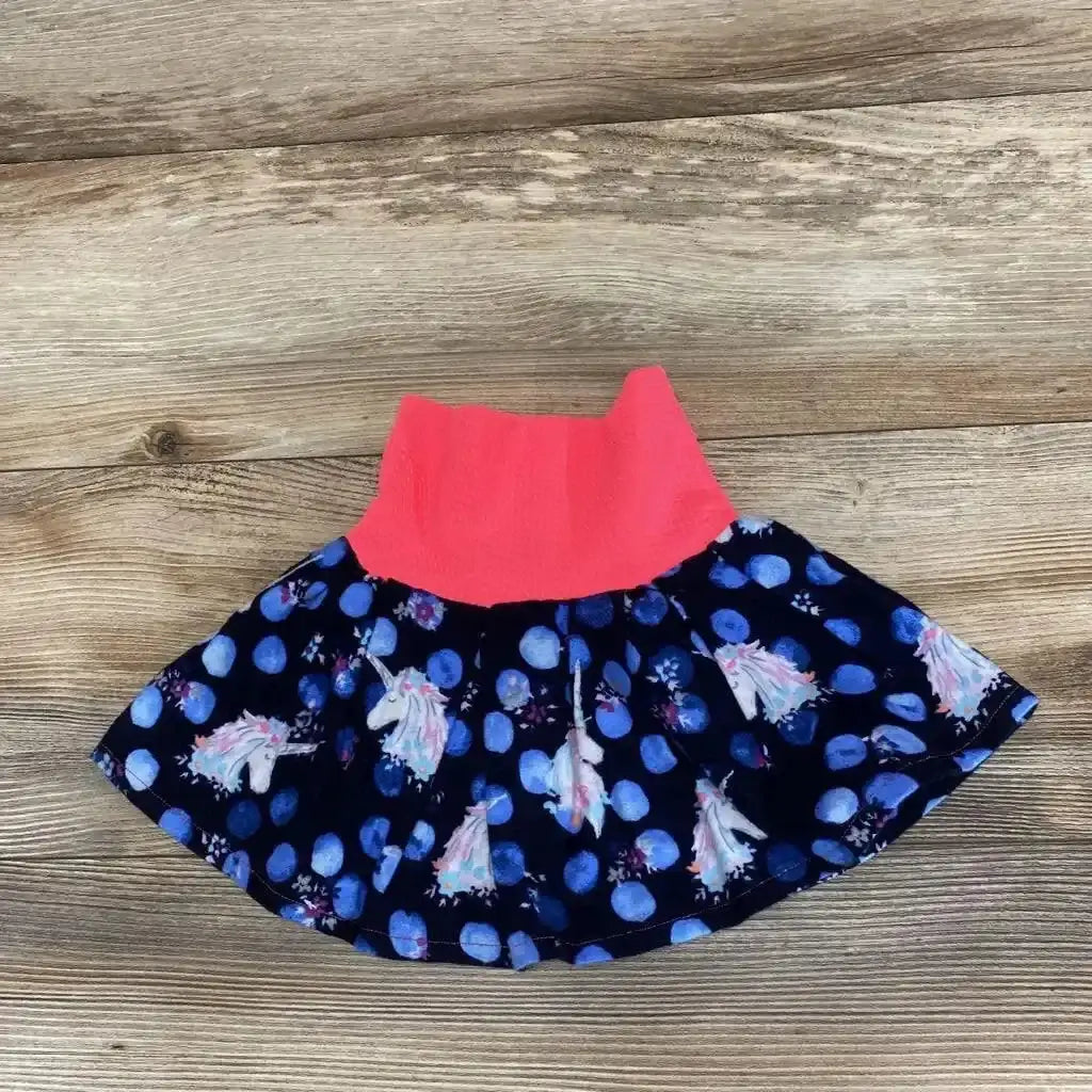 Flat lay of navy infant unicorn skirt (3-6 months) with coral ribbed waistband and unicorn-and-blue-dot print on wooden floor