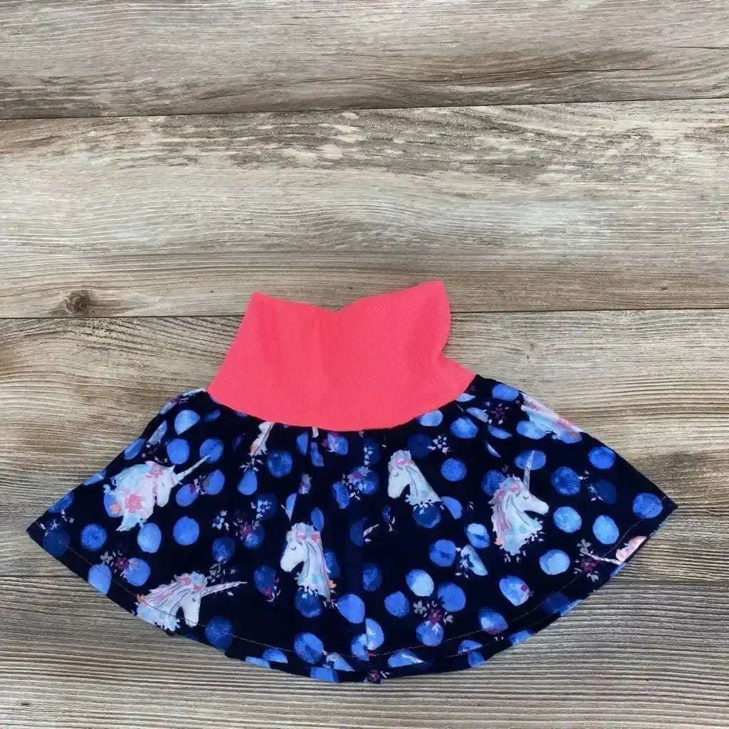 Flat lay of baby unicorn skirt size 3-6 months, navy polka dot and unicorn print with coral elastic waist on wood background