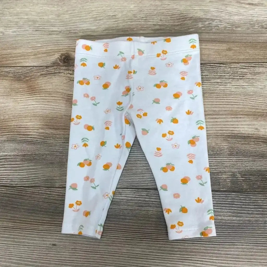 Flat lay of white baby pants with orange fruit and pink floral print showing elastic waistband on wood background