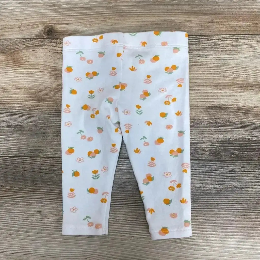 Front flat-lay of white baby leggings (6 months) showcasing orange fruit and peach floral print with light wood background