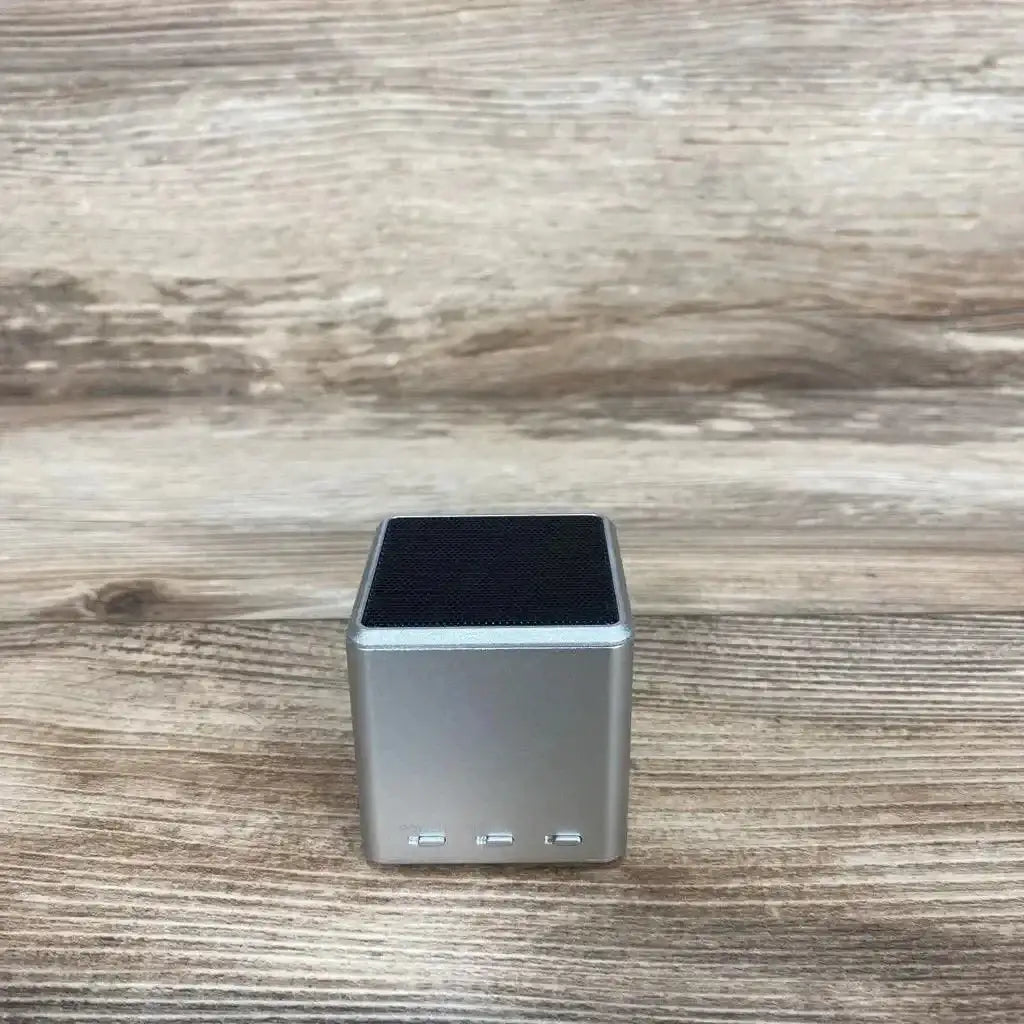 Front view of grey cube Lullabuddy portable speaker showing black mesh top and three front control buttons on wood background