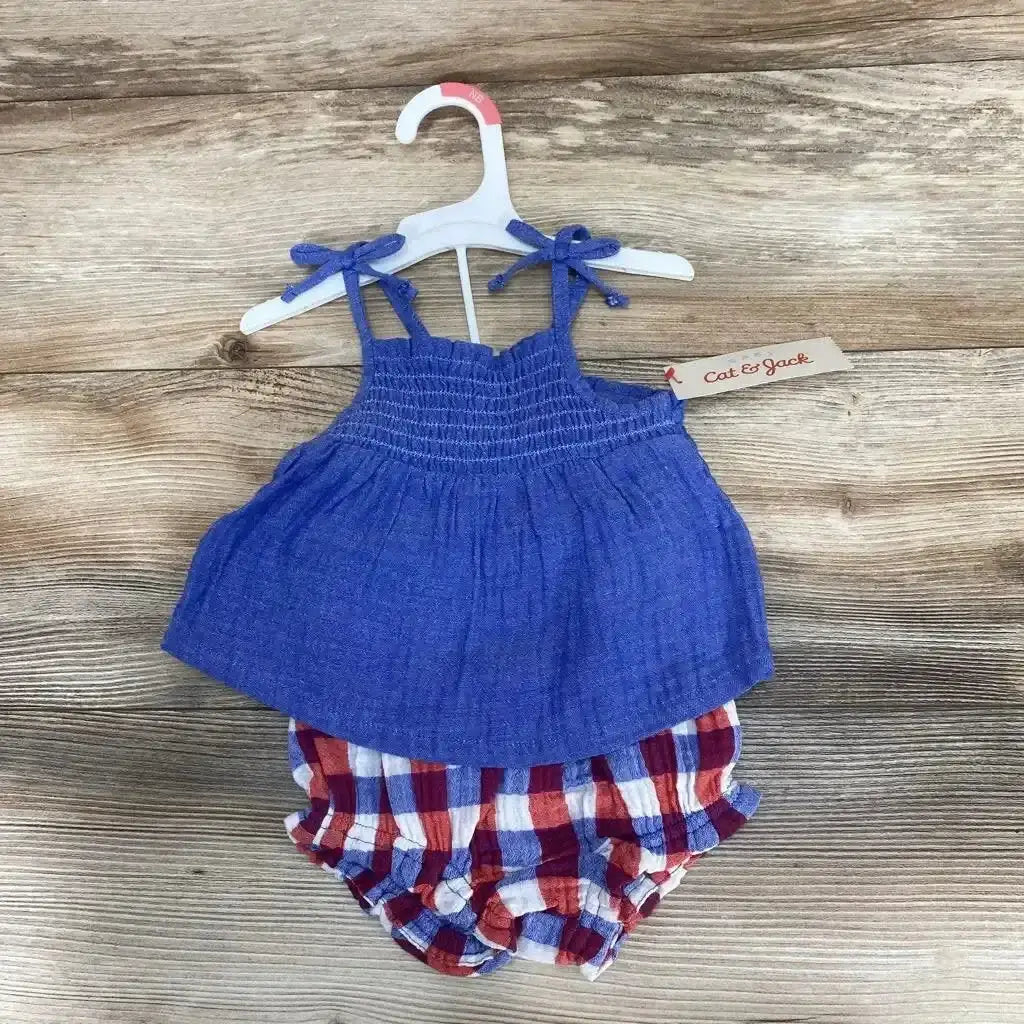 Flat lay of Cat & Jack smocked blue top with tie straps and red-white-blue plaid bloomers, size 3-6 months on wooden floor