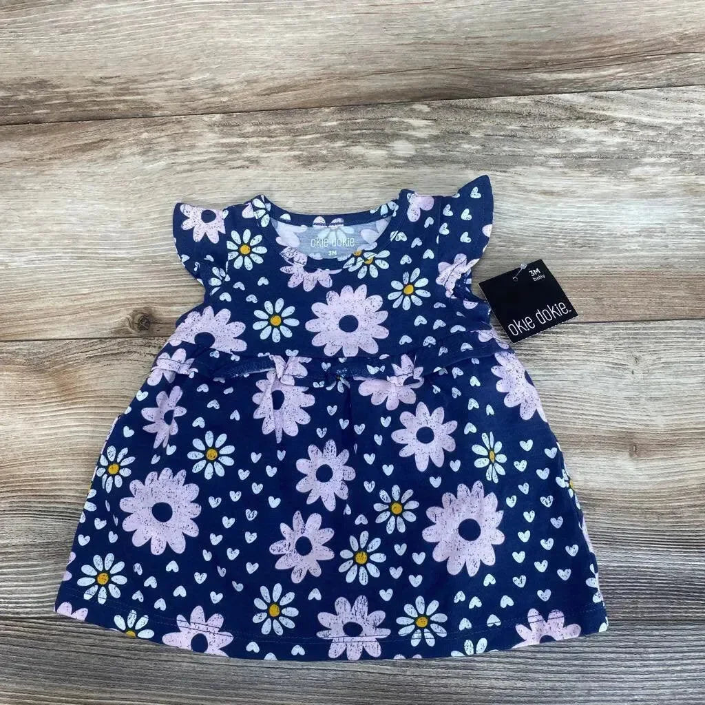 Front view of Okie Dokie navy baby dress and bloomers showcasing pink daisy print and flutter sleeves, size 3M on wood floor