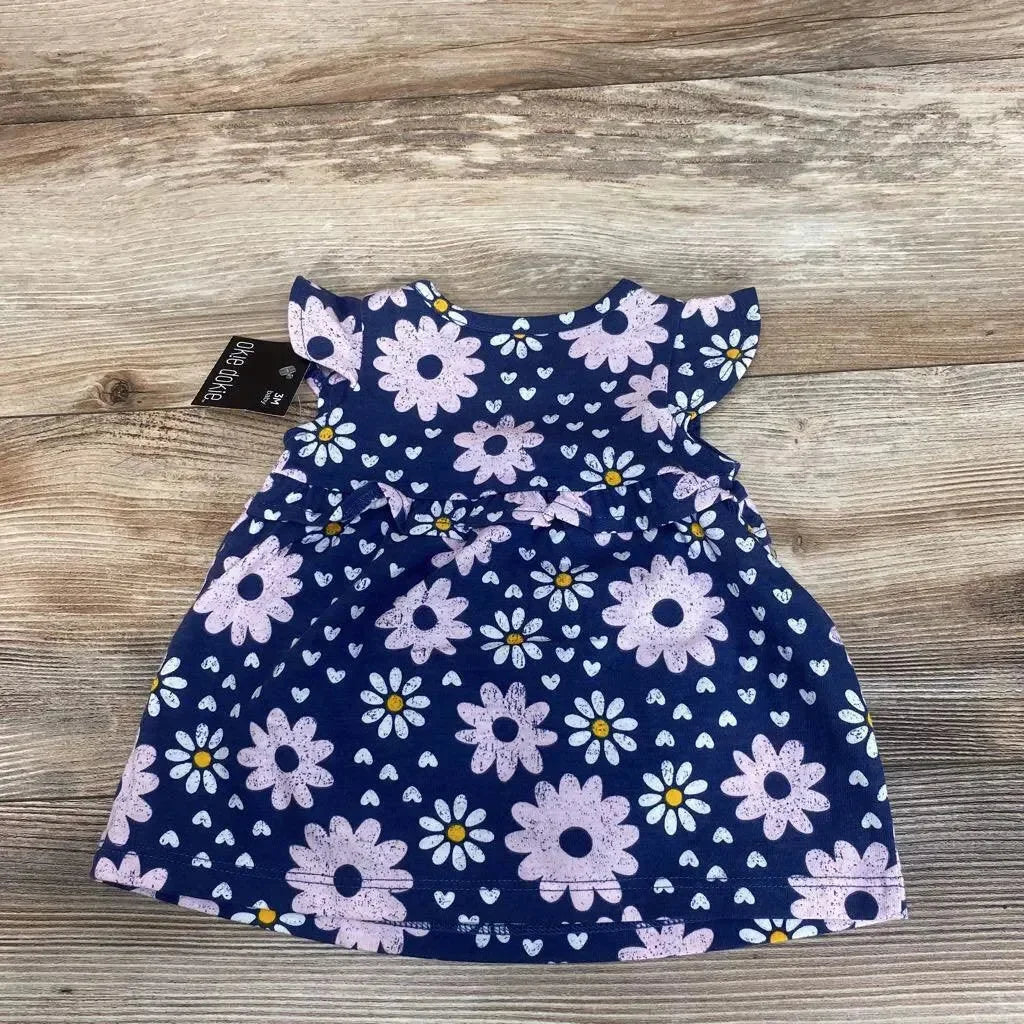 Front flat lay of navy baby dress showing pink and white daisies, flutter sleeves and ruffle waist on wood background
