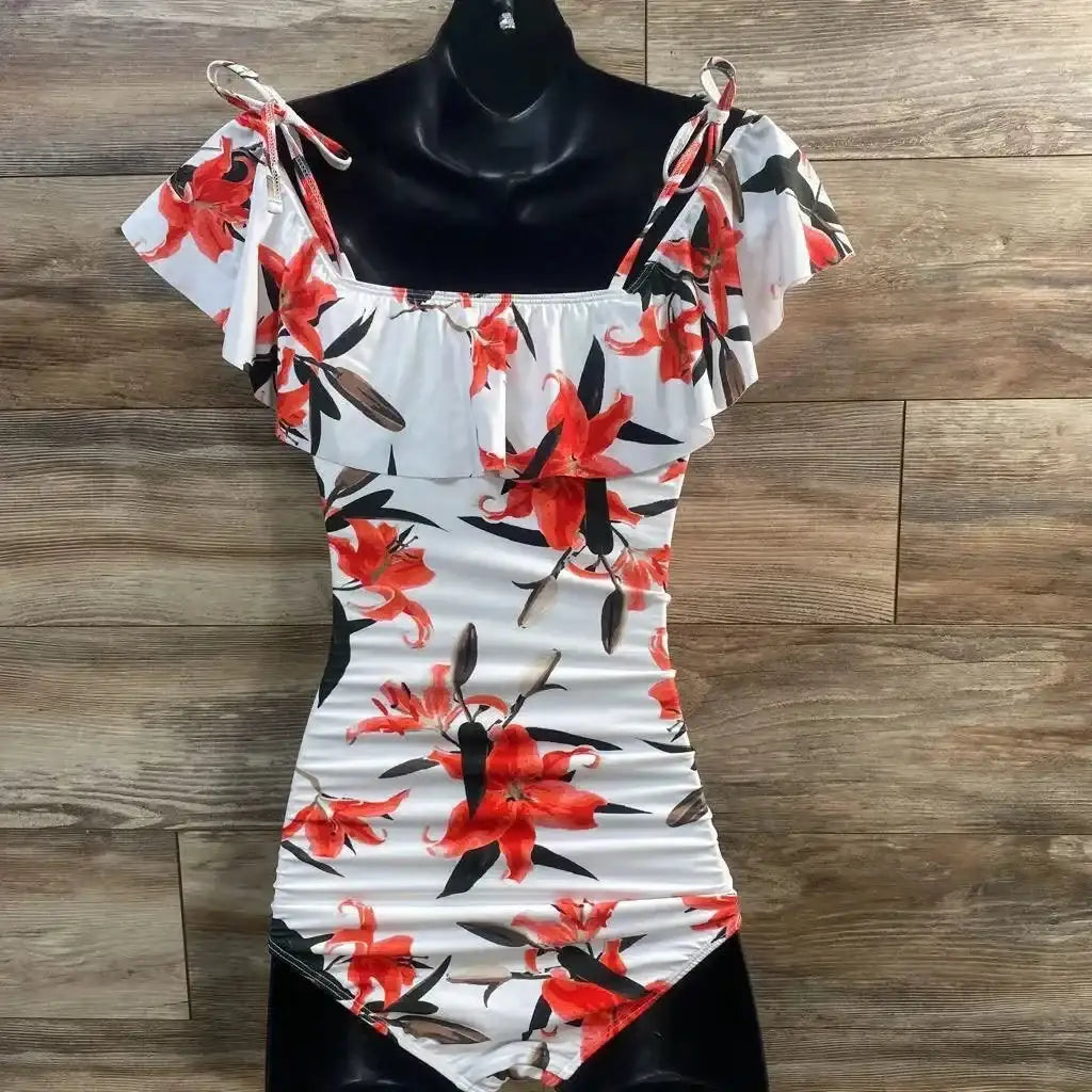 Front view of white one-piece swimsuit with red floral, off-shoulder ruffle, tie straps and side ruching on wood background