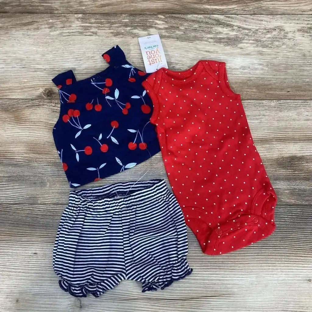 Flat lay of 3-piece baby set: red polka dot bodysuit, navy cherry tank, and navy striped ruffle shorts on wood background