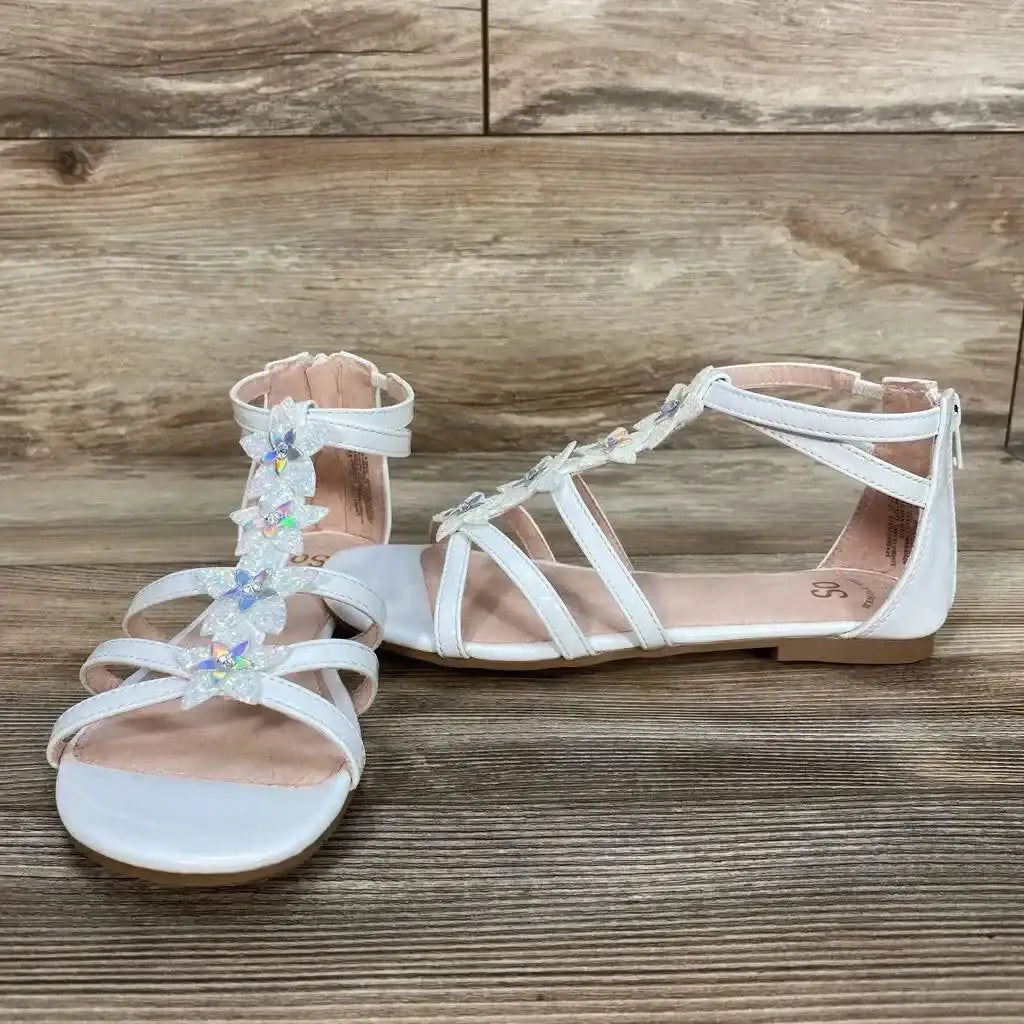 Three-quarter view of NEW SO Loganberry Gladiator Sandals sz 4Y in white with iridescent flower embellishments back zip and ankle strap on wood plank floor