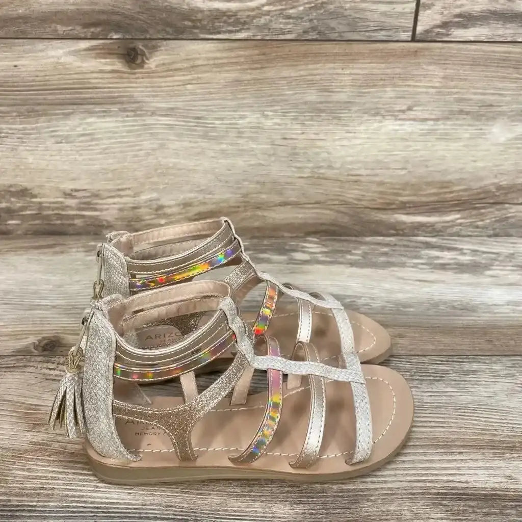 Three-quarter view of Arizona Jean Co Angel gladiator sandals in metallic gold with rainbow jewel strap and back zip on wood floor