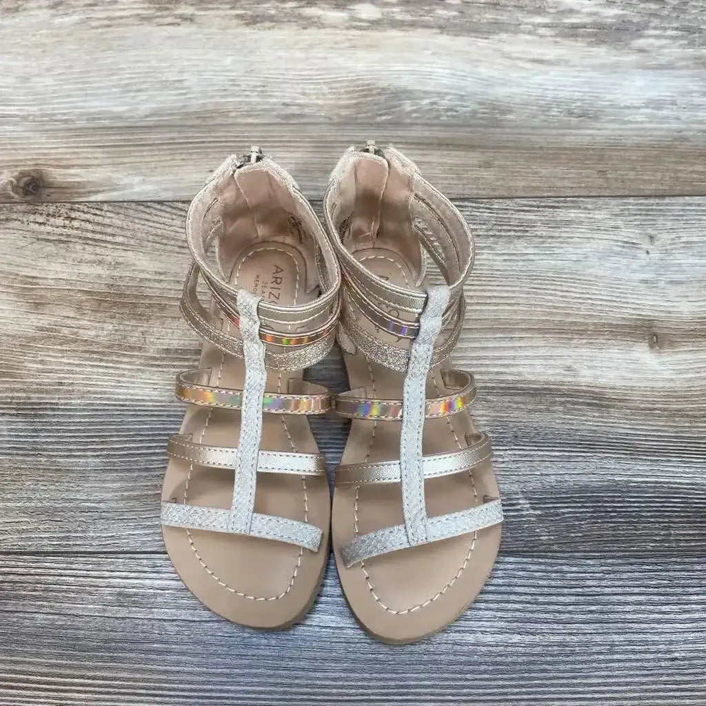 Top view of Arizona Jean Co Angel gladiator sandals in rose gold with metallic and iridescent straps on wood plank background