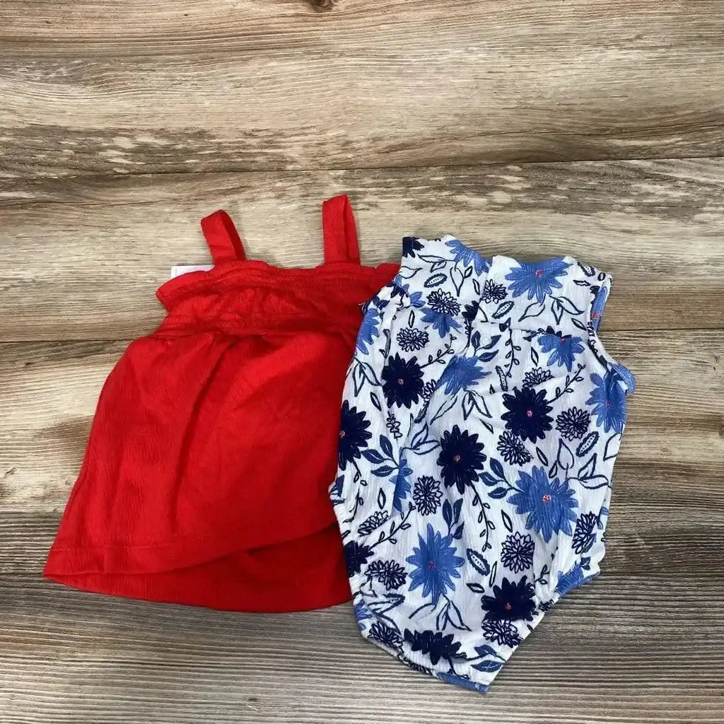 Flat lay of baby romper set showing a red sleeveless dress and a white romper with blue floral print on wood background