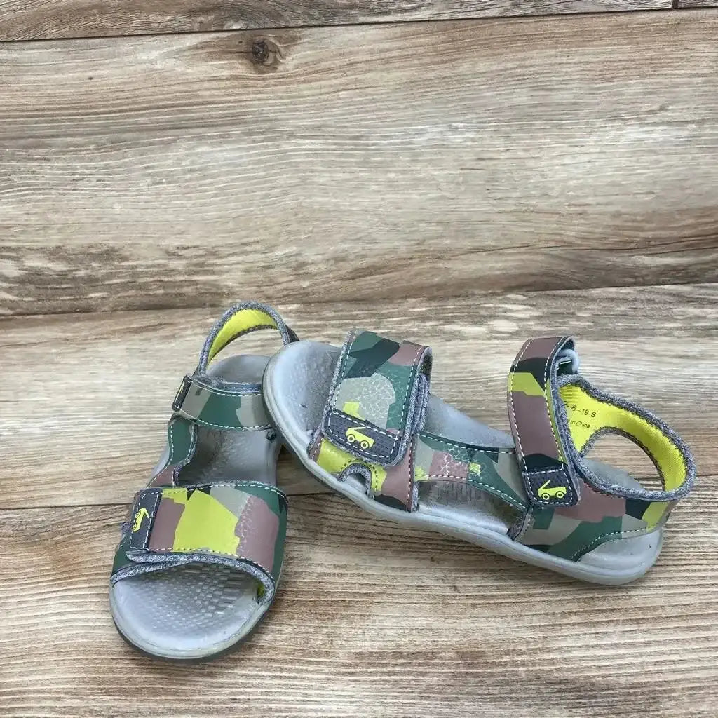 Three-quarter view of See Kai Run Billie Flexirun toddler sandals, green camo with yellow lining and two Velcro straps on wood background