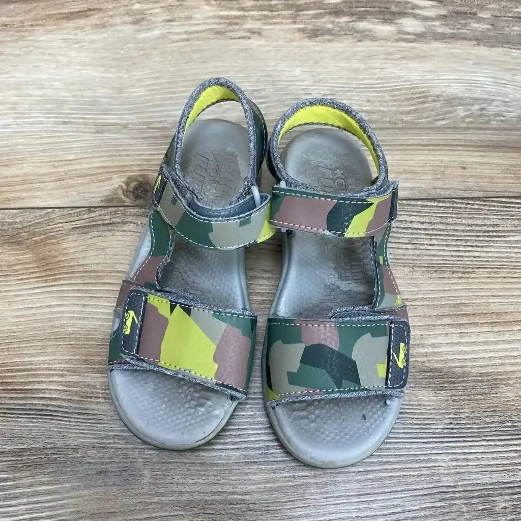 Top view of See Kai Run Billie toddler sandals, green camouflage with Velcro straps and worn footbeds on wood floor, size 12C