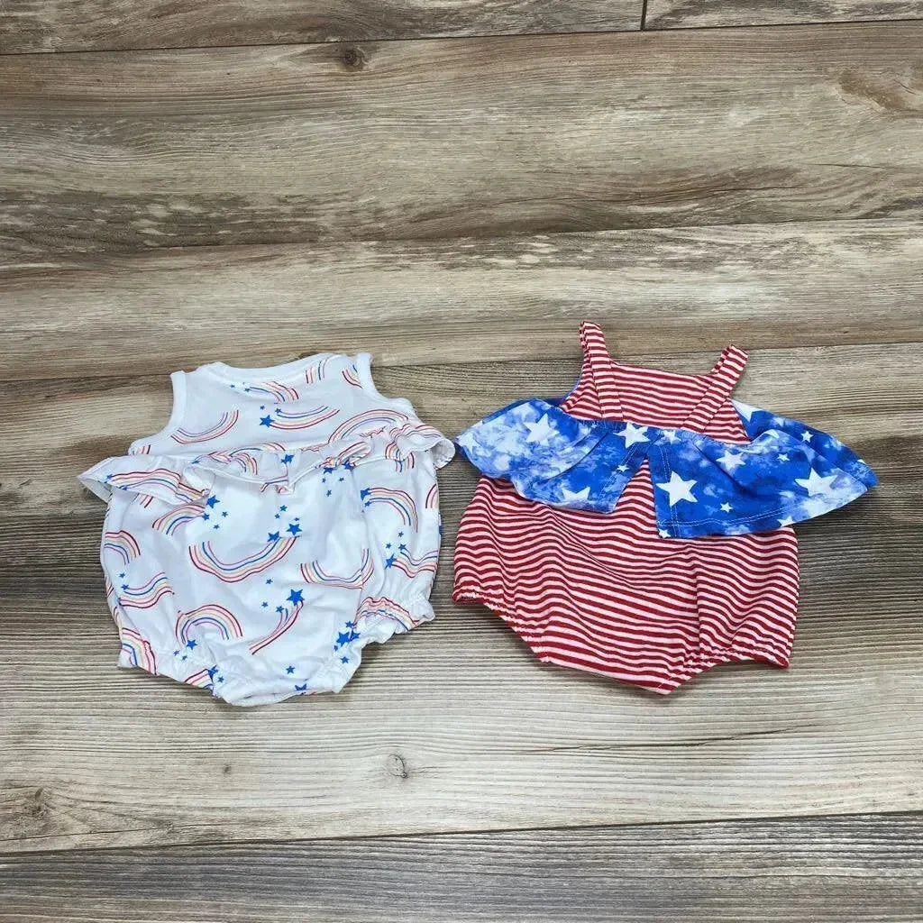Top-down view of two newborn rompers: white rainbow-and-star romper and red striped romper with blue star ruffle on wood background