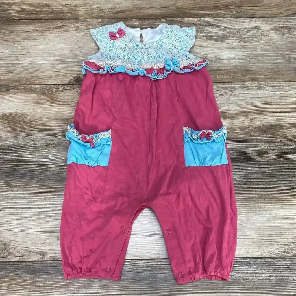 Flat lay of pink cap-sleeve ruffle romper showcasing lace yoke, blue ruffle-trim pockets and crotch snaps on wood background