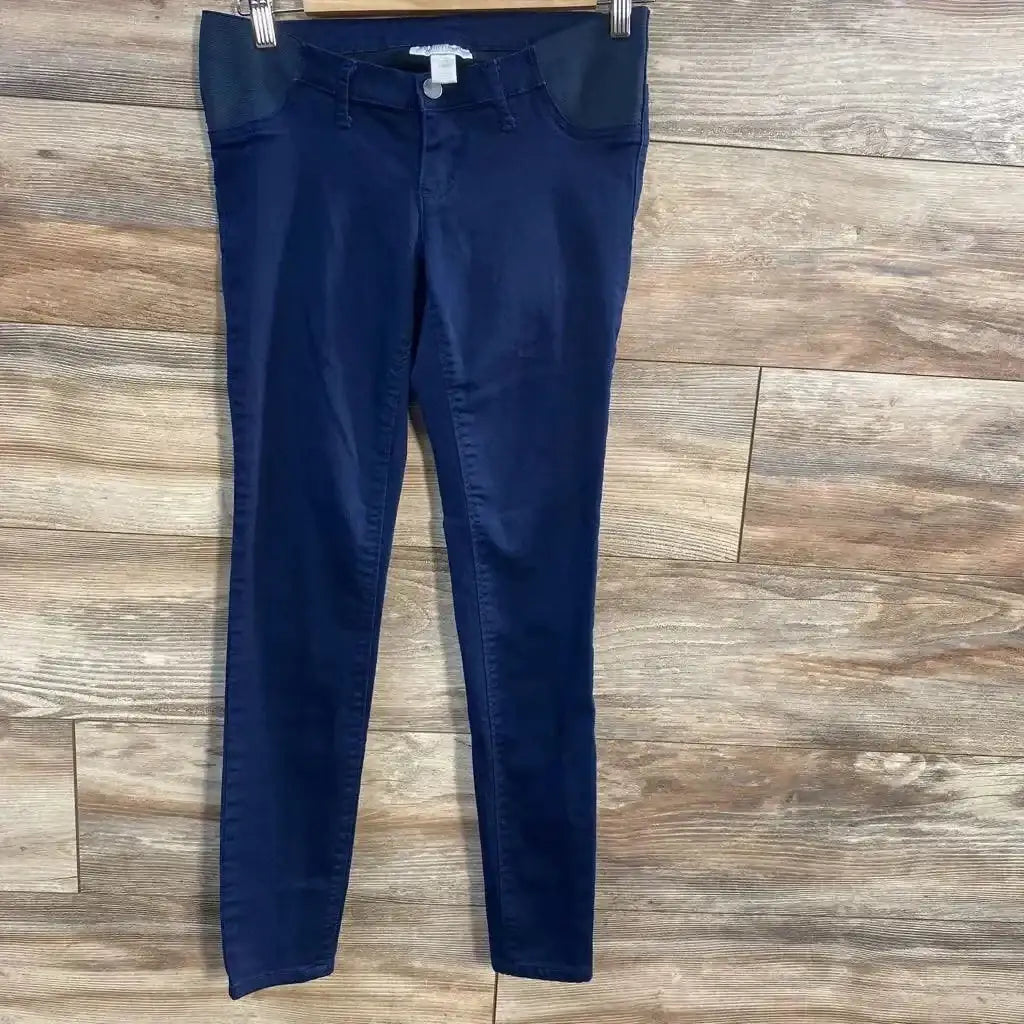 Front view of navy Motherhood Maternity side-panel pants showing elastic side panels and slim legs on wood-plank background