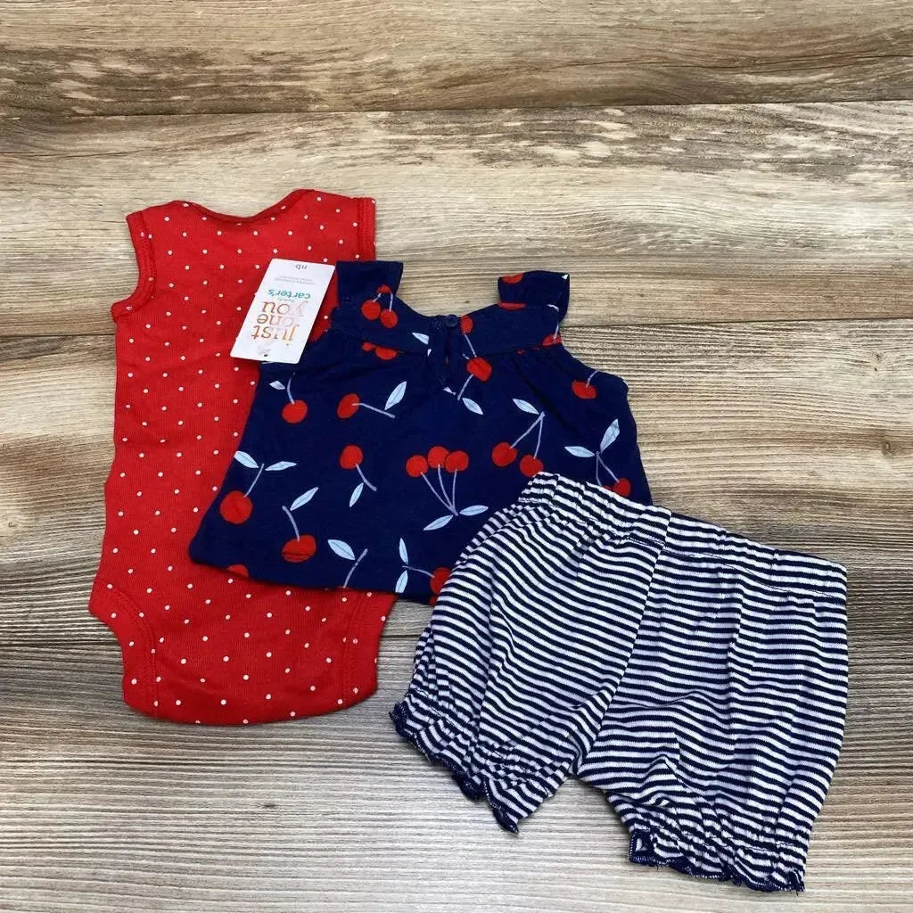 Flat lay of newborn three-piece set: red polka-dot bodysuit, navy cherry-print tank, navy-and-white striped shorts on wood background