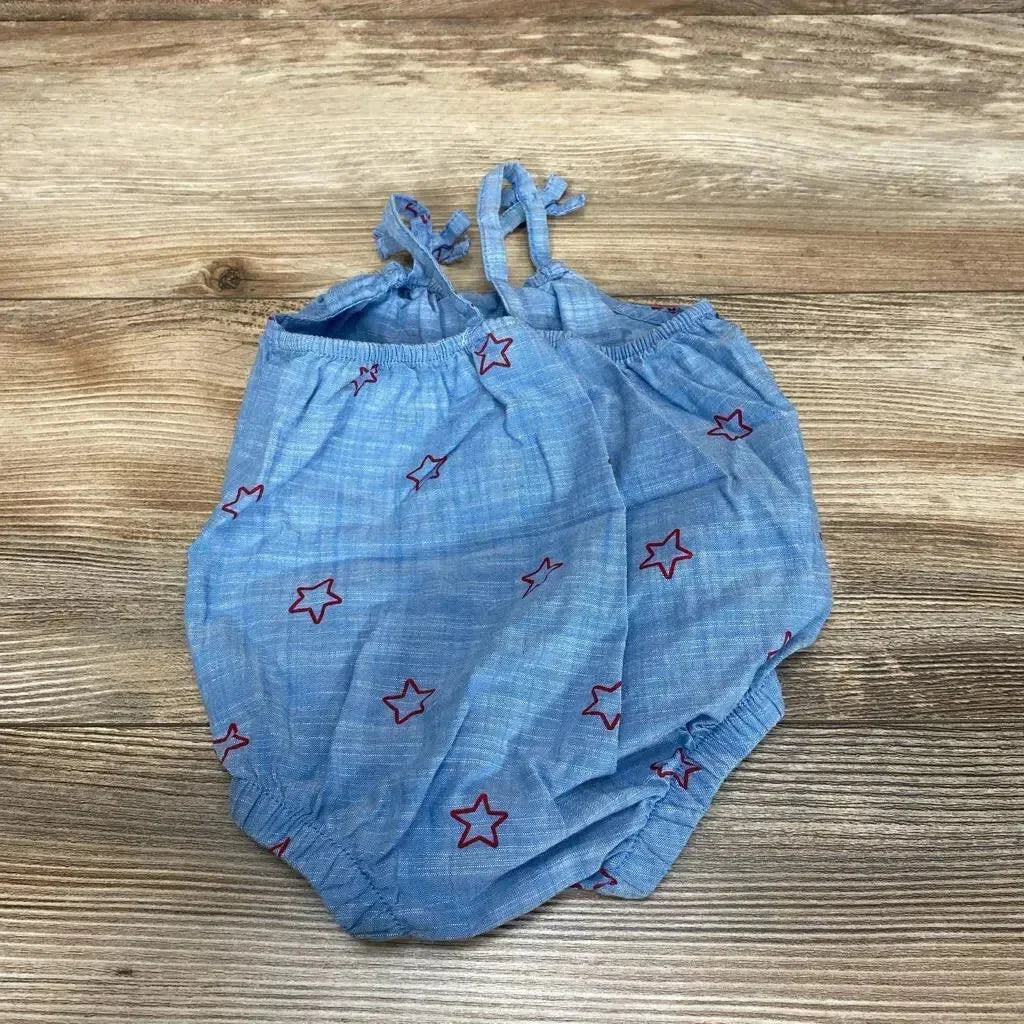 Flat-lay of blue chambray baby romper with red star embroidery, tie straps and elastic leg openings on wood background