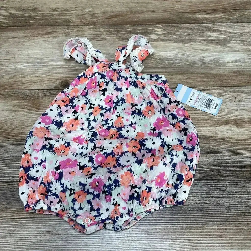 Top-down view of pink floral baby romper (0-3 months) showcasing flutter sleeves and snap closures on a wood background