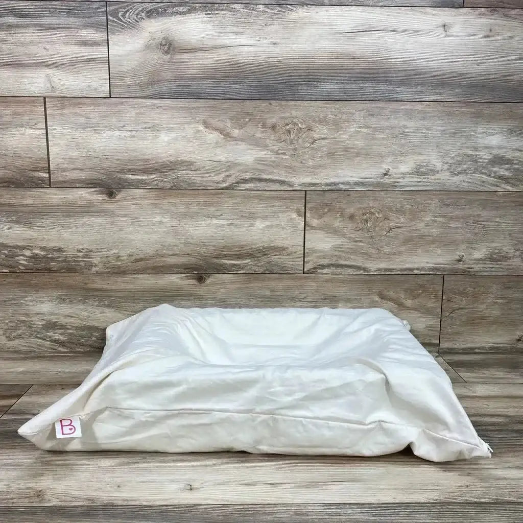 Side view of ivory Belly Baby breast pregnancy pillow showing lowered center and removable cover on wood-plank backdrop