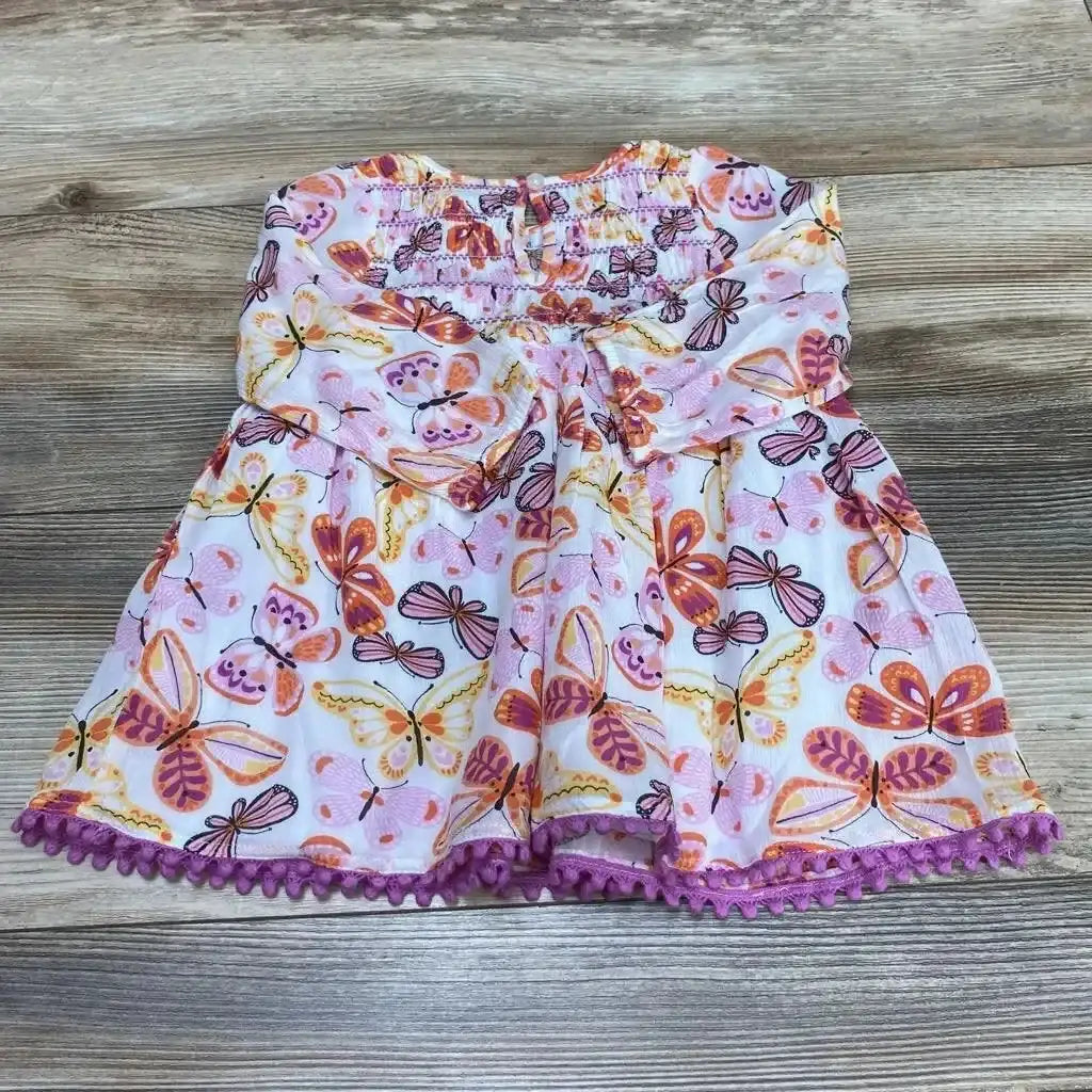 Flat lay of baby smocked dress showcasing smocked bodice and purple pom-pom trim with pink and orange butterfly print on wood background