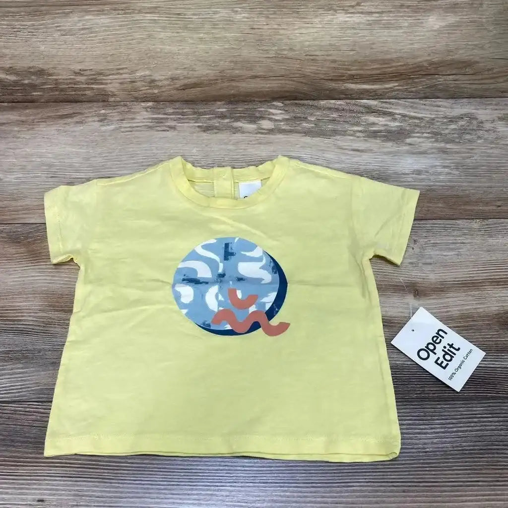 Flat lay of yellow 12m baby t-shirt showing round blue-white abstract print with pink squiggle on wood backdrop