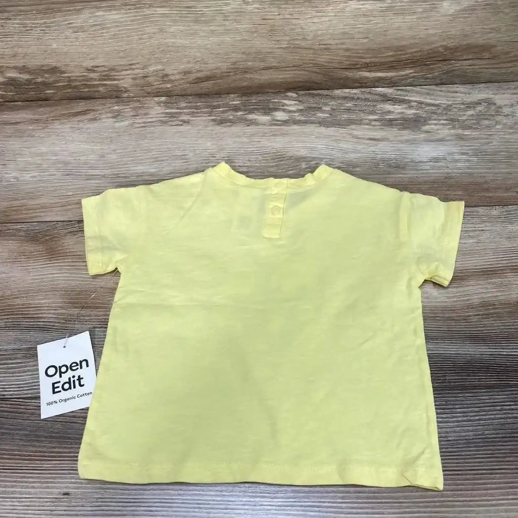 Back view of new Open Edit organic graphic t-shirt in yellow with two-button placket and 100% organic cotton hangtag on wood plank floor
