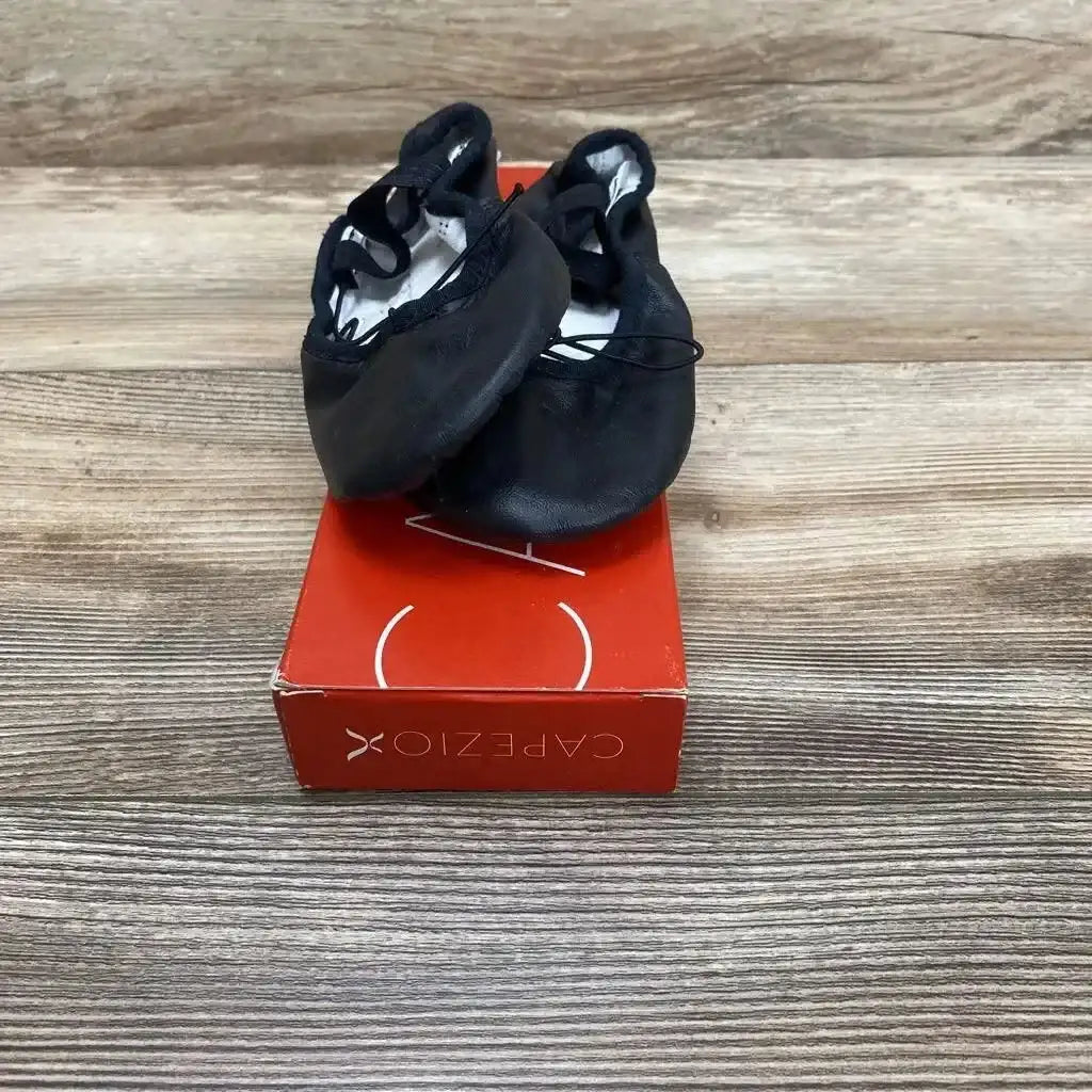 Front view of black Capezio Daisy 205 ballet shoes showing elastic straps and light wear, on a red Capezio box on wood