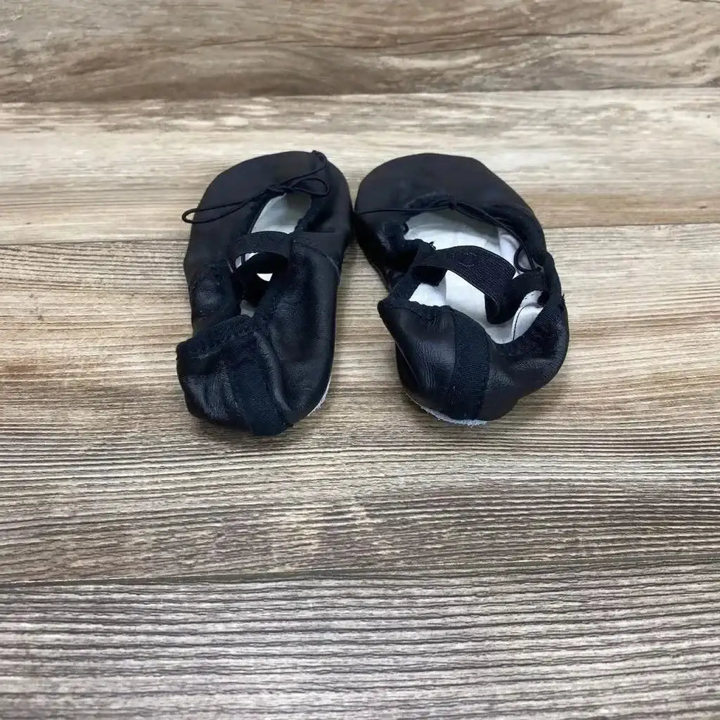 Top-down view of used black Capezio ballet shoes, toddler size 1.5M, showing elastic straps and worn soles on wood background