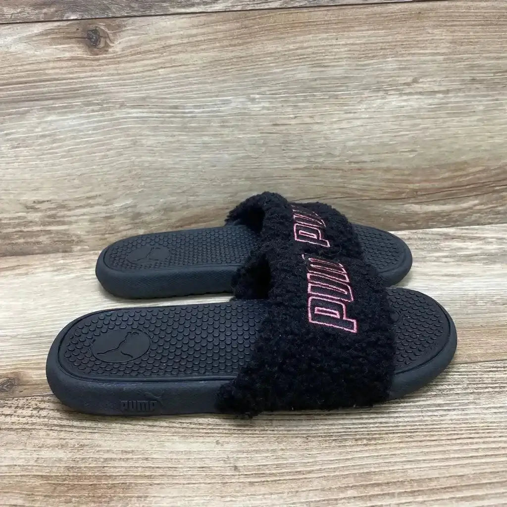 Three quarter view of Puma Cool Cat sherpa slides in black with pink PUMA embroidered logo on wood plank floor