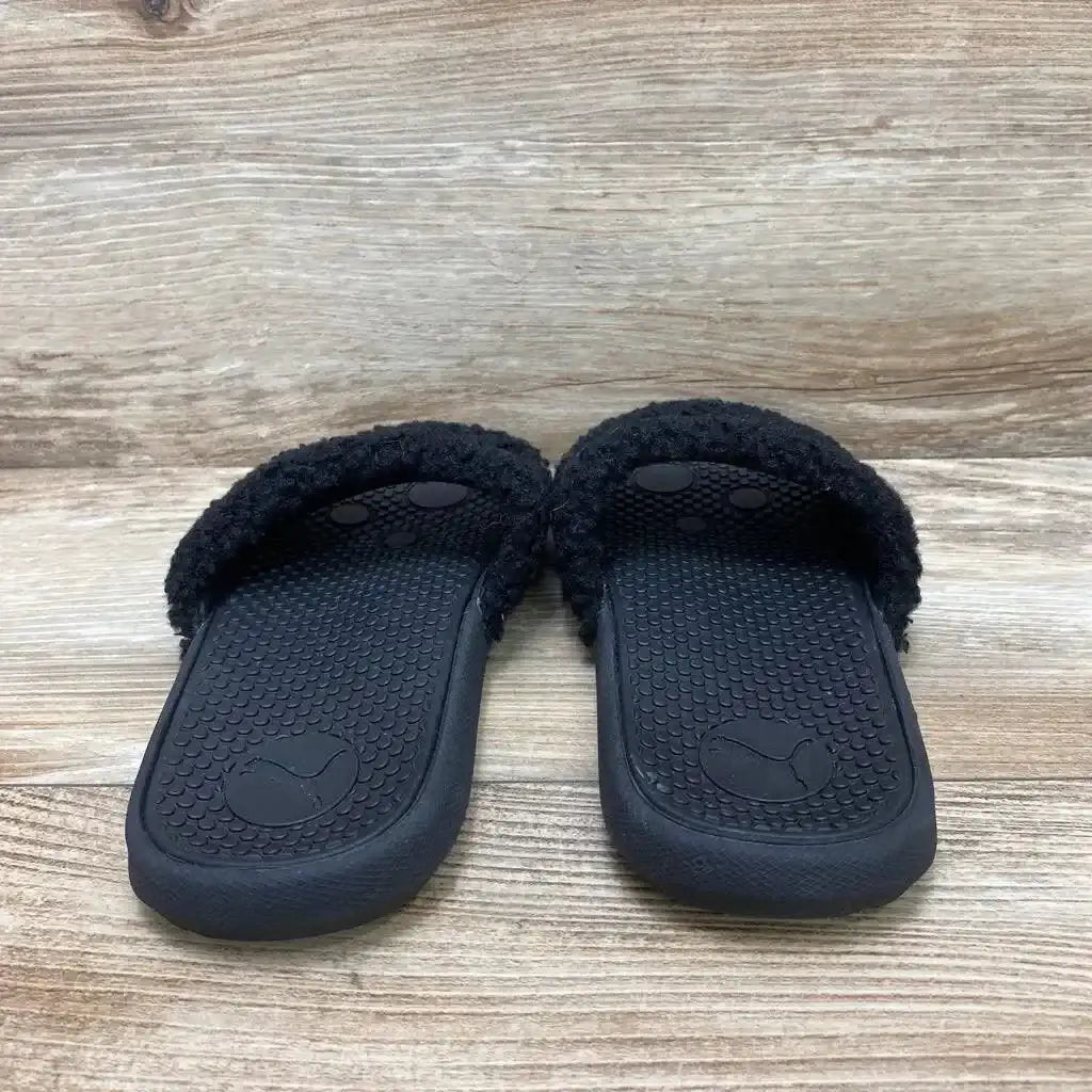 Front view of pair of black Puma Cool Cat Sherpa slides size 3Y showing fuzzy sherpa strap and textured footbed on wood background