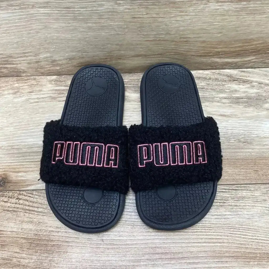 Top view of Puma Cool Cat Sherpa Slides sz 3Y showcasing black sherpa straps with pink Puma logo embroidery on wood plank background