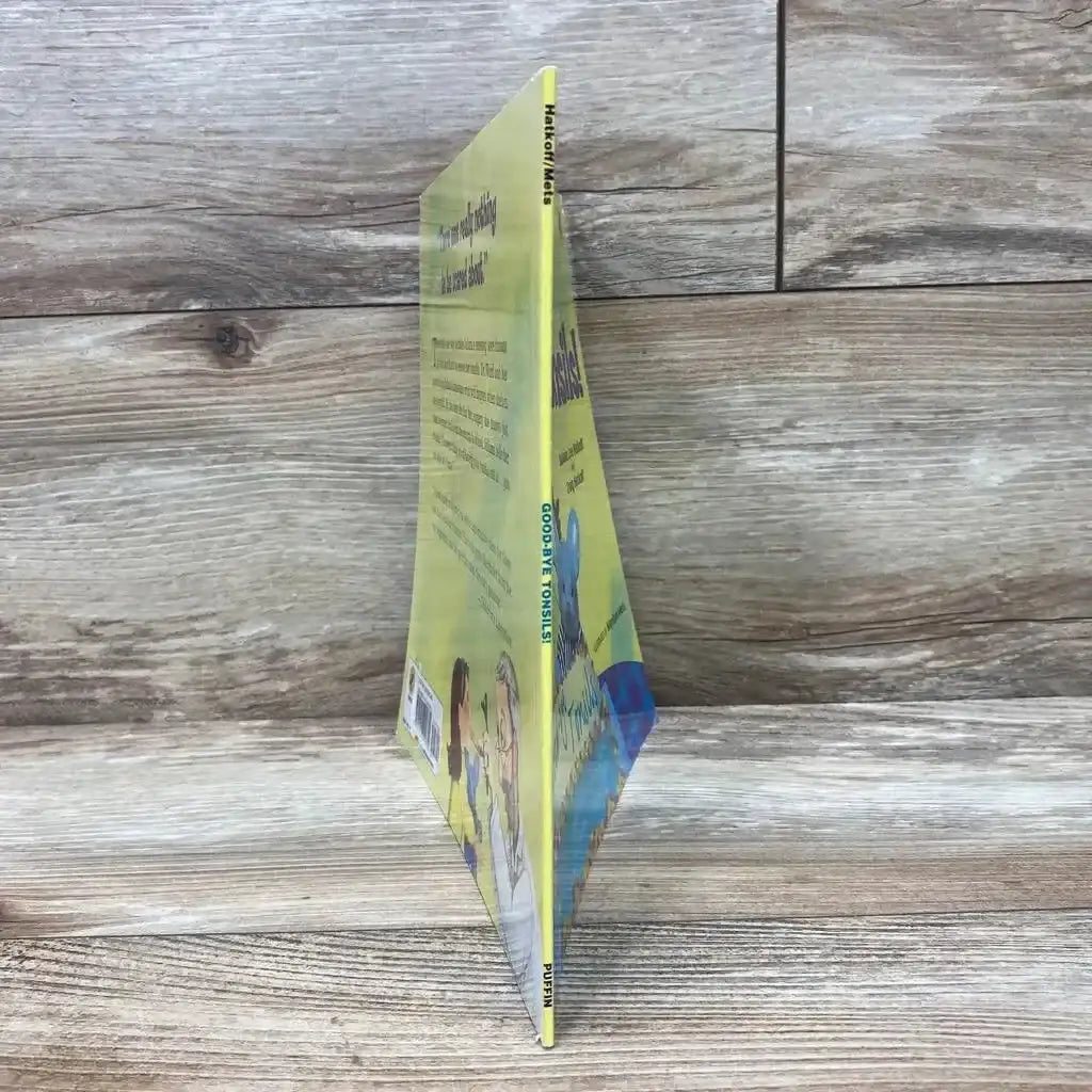 Angled view of Good-bye Tonsils! paperback book showcasing its yellow illustrated cover on a wood-grain surface