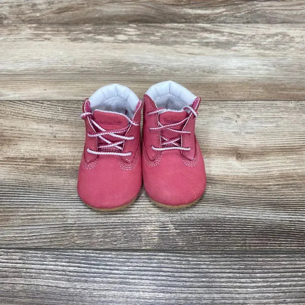 Front view of Timberland infant crib booties (size 1C) showcasing pink suede upper, white padded lining and lace detail on wood plank background