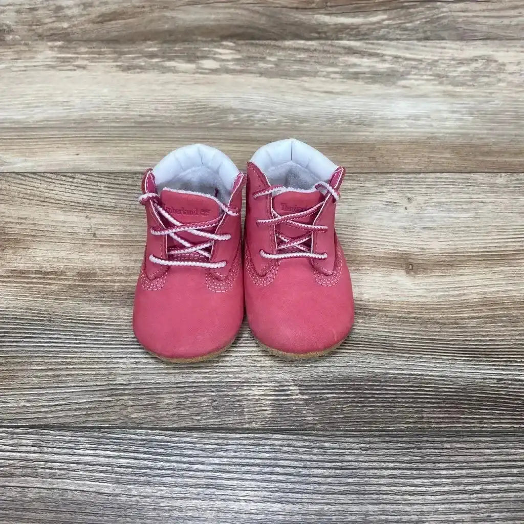 Front view of Timberland infant crib booties (size 1C) showcasing pink suede upper, white padded lining and lace detail on wood plank background