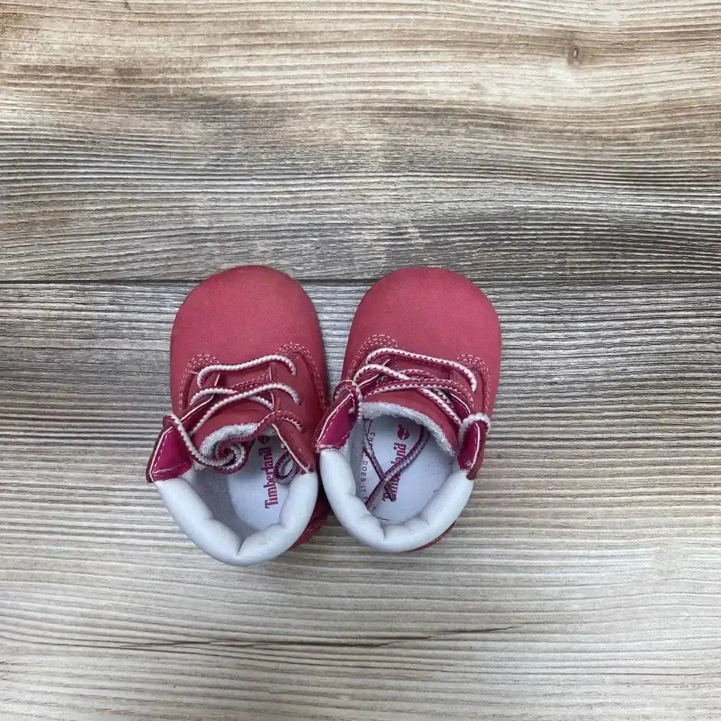 Top view of pink Timberland infant crib booties, size 1C, showing padded white ankle collars and laces on light wood background