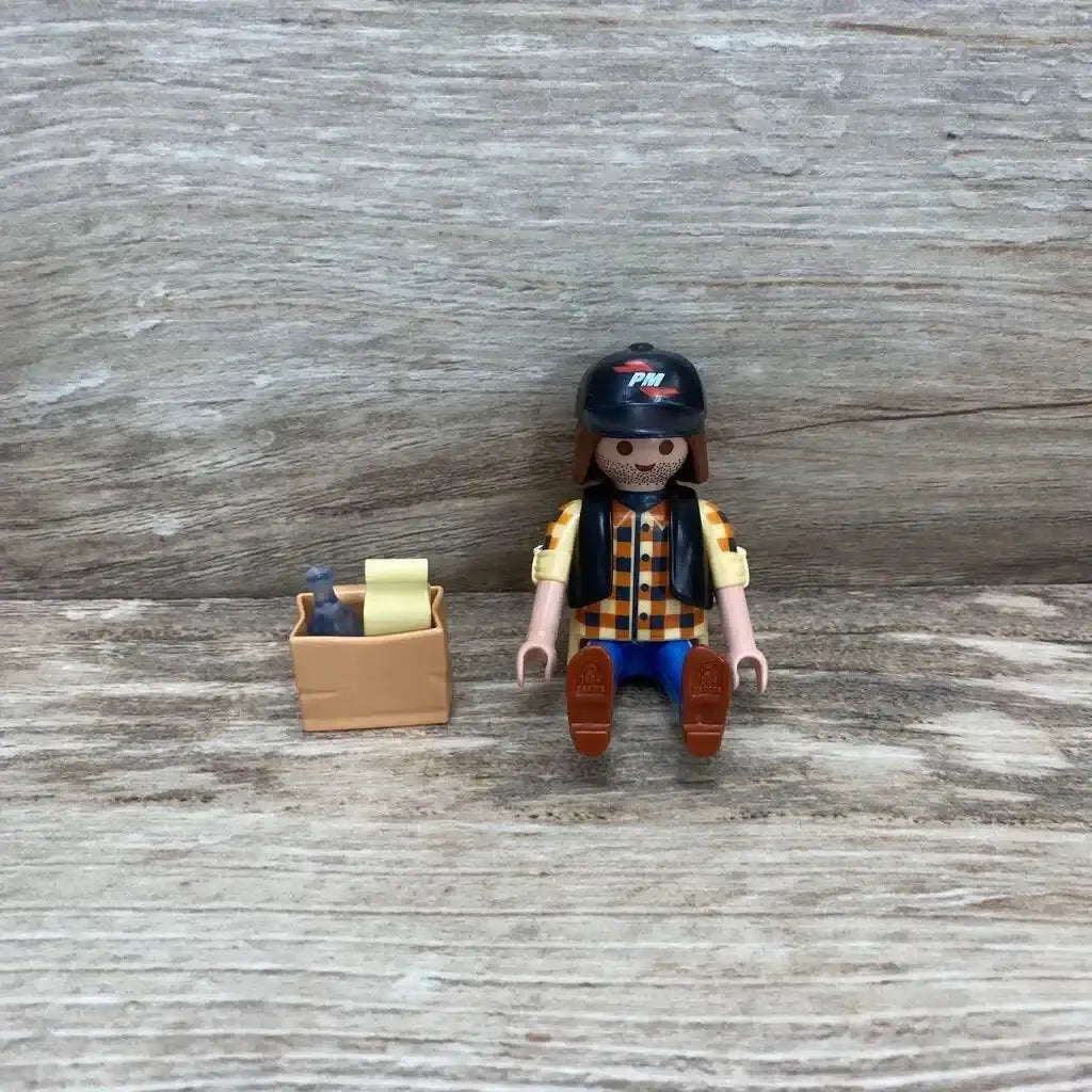Front view of Playmobil dump truck driver figure with black helmet and checkered shirt and tan crate on wood background