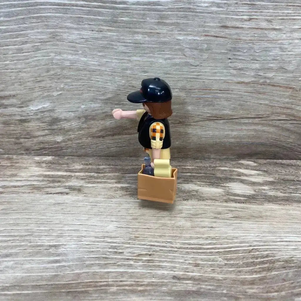 Side view of Playmobil 5665 dump truck driver figure with black cap and vest holding a tan crate on wood background