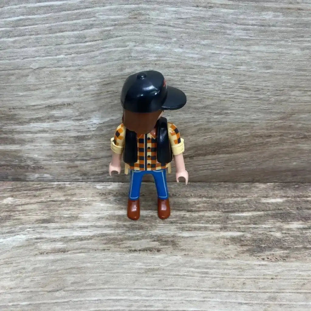 Front view of Playmobil 5665 dump truck driver figure wearing black cap and checkered shirt on woodgrain background