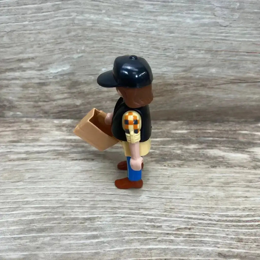 Side view of Playmobil 5665 dump truck driver figure showcasing black cap blue pants and accessories on wood plank floor