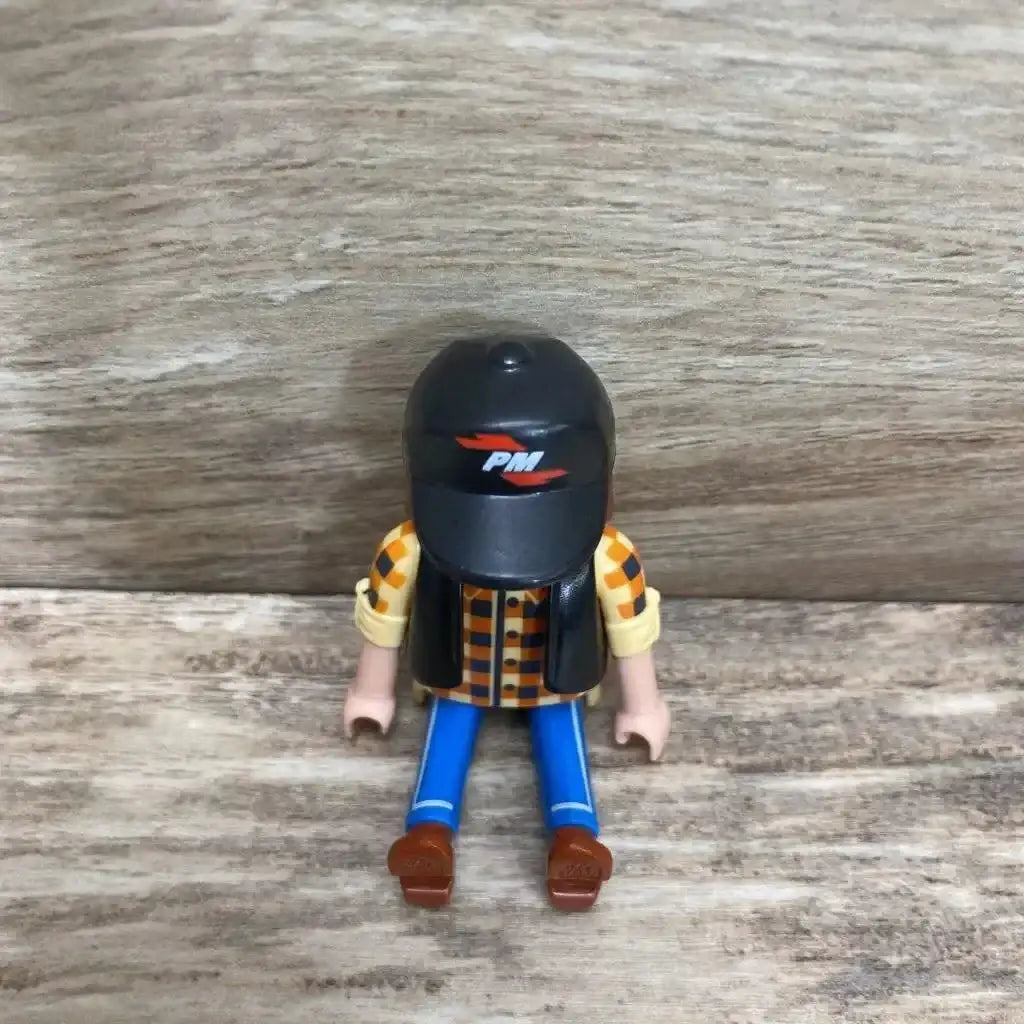 Front view of Playmobil 5665 dump truck driver wearing black helmet with PM logo, orange checked shirt and blue pants on wood background