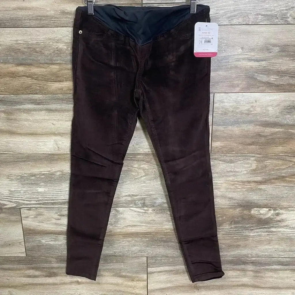 Front view of burgundy Isabel maternity crossover-panel skinny jeans showing crossover belly panel and tapered, tapered legs on wood floor background