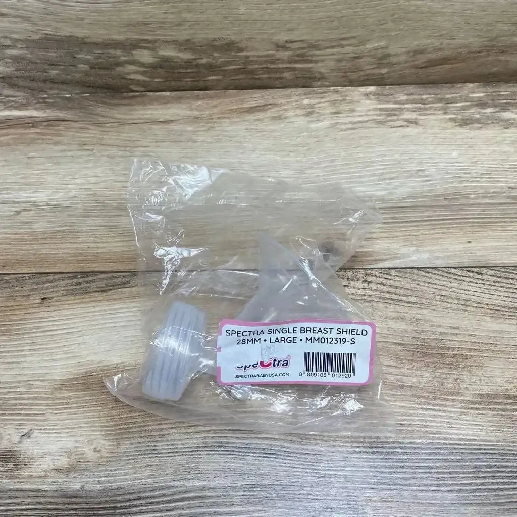 Top-down view of Spectra 28mm breast pump flange in clear plastic packaging with white connector ring on light wood surface