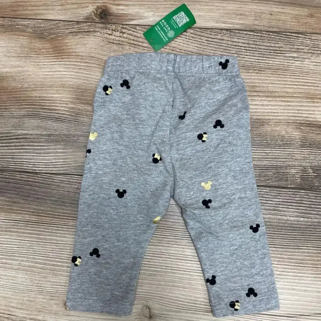Front flat-lay of grey BabyGap baby leggings with black and gold Mickey head prints and elastic waistband on wood background