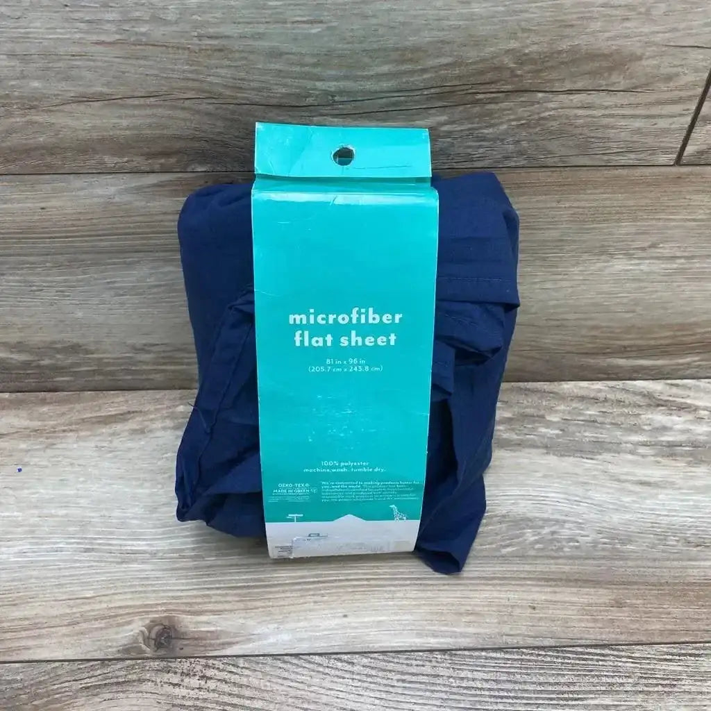 Front view of Pillowfort microfiber flat sheet in navy in teal retail wrap labeled 81 in x 96 in on wood plank floor