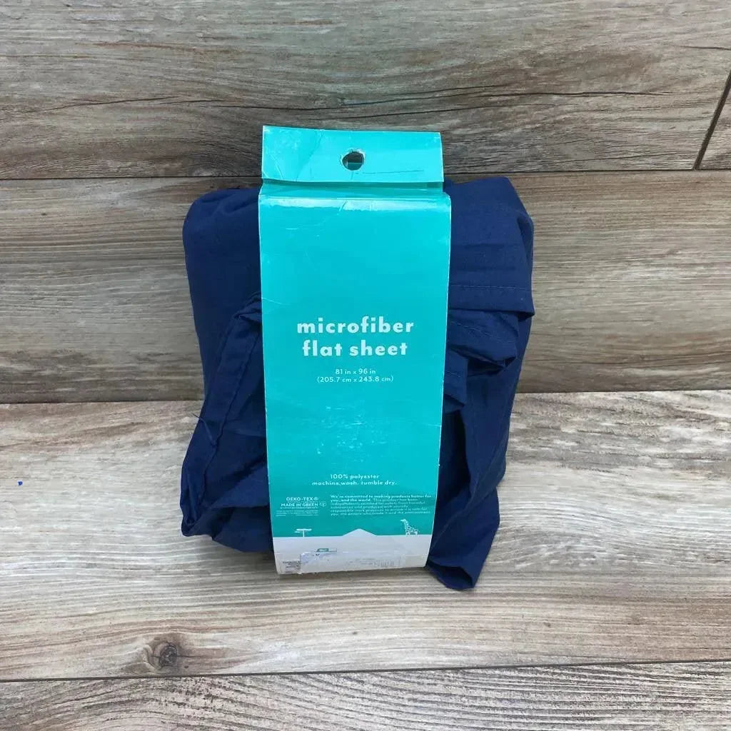 Front view of folded navy Pillowfort microfiber flat sheet with teal label showing 81 x 96 in on light wood