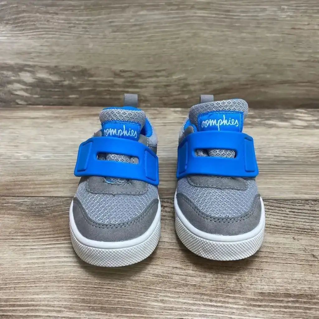 Front view of grey toddler Oomphies Devon sneakers, size 7C, showing blue Velcro strap and white rubber sole on wood background