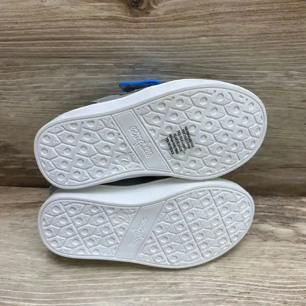 Bottom view of Oomphies Devon toddler sneakers (size 7C) showing white textured rubber soles and brand imprint on wood background